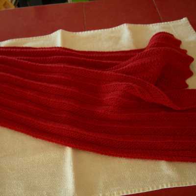 Red Chevron Scarf, sitting folded in half with ends fanned out on white towel on top of red table