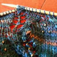 closeup of blue variegated lace knitting with beads and nupp on needles