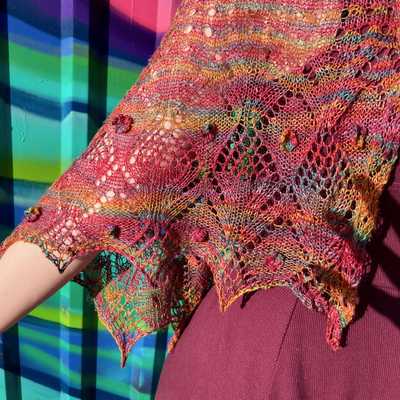 closeup of brightly colored lace shawl showing crochet flower detail, in front of bright graffiti style wall