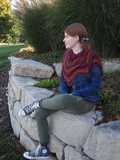 another angle of Rosita shawlette wrapped around shoulders kerchief style, with model sitting on edge of rock wall with feet positioned to show off sneakers