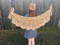 model holding speckled Feuille-morte shawl between her hands to show flat shape, also matching hat on head