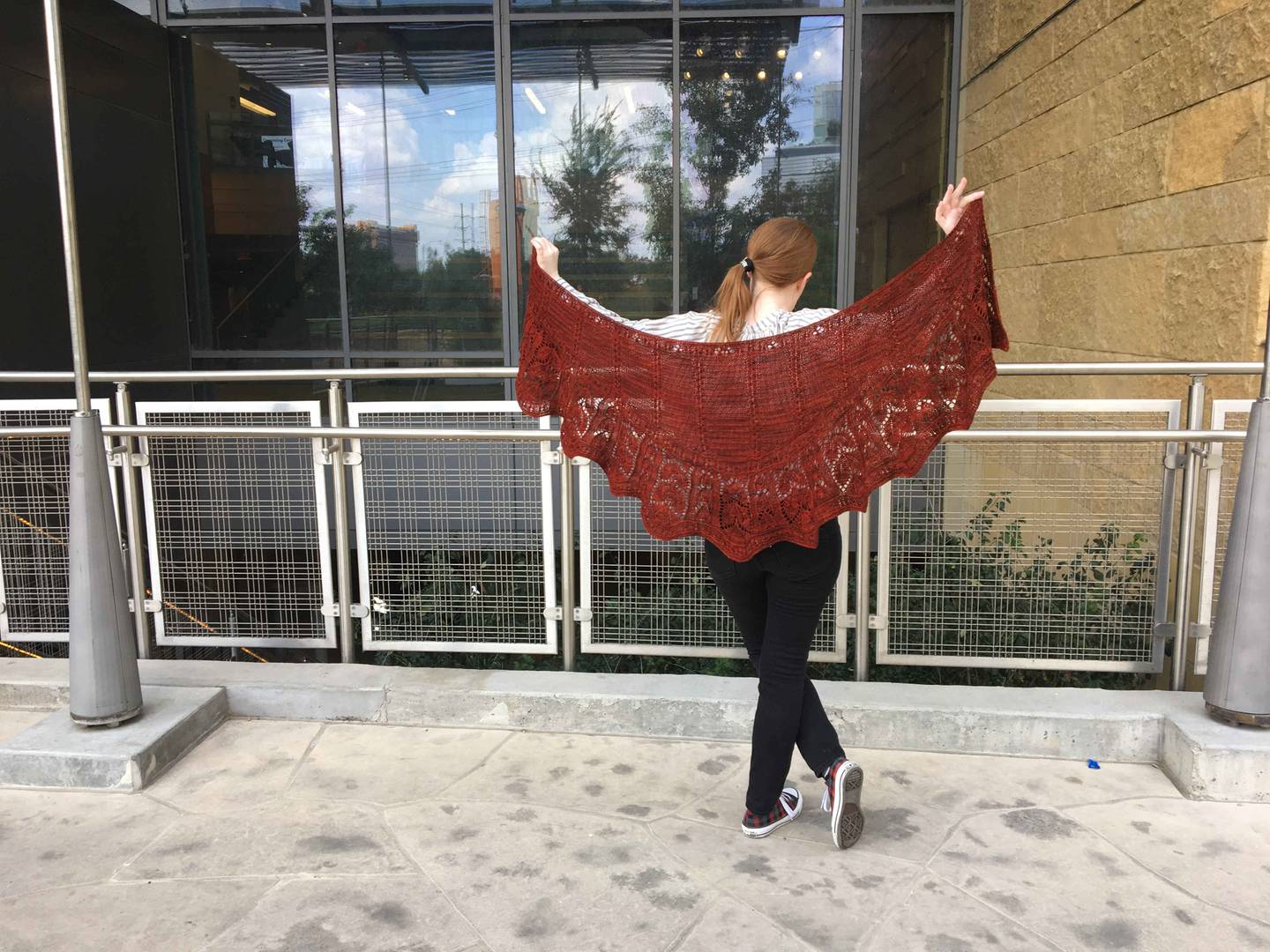 woman holding dark red crescent-shaped shawl suspended between her hands, and standing in front of railing at Austin Public Library