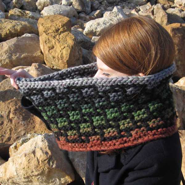 woman holding top edge of larger Carreau cowl to illustrate the larger circumference and show off the gradient colors of the bulky mosaic pattern